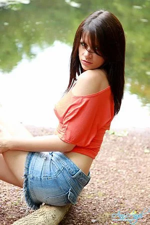 Sweet Ann Angel in blue jean mini skirt and red t-shirt spreads poses on the bank of the river