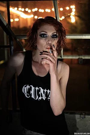 Photographic art model and raunchy redhead Virginia Mae smokes a cigar while posing.